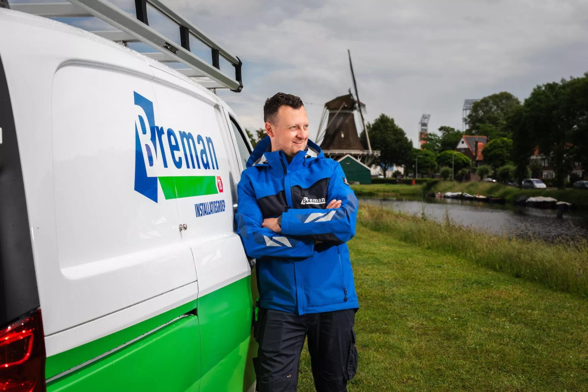 Breman medewerker bij een Breman bus met op de achtergrond een dorp en molen.