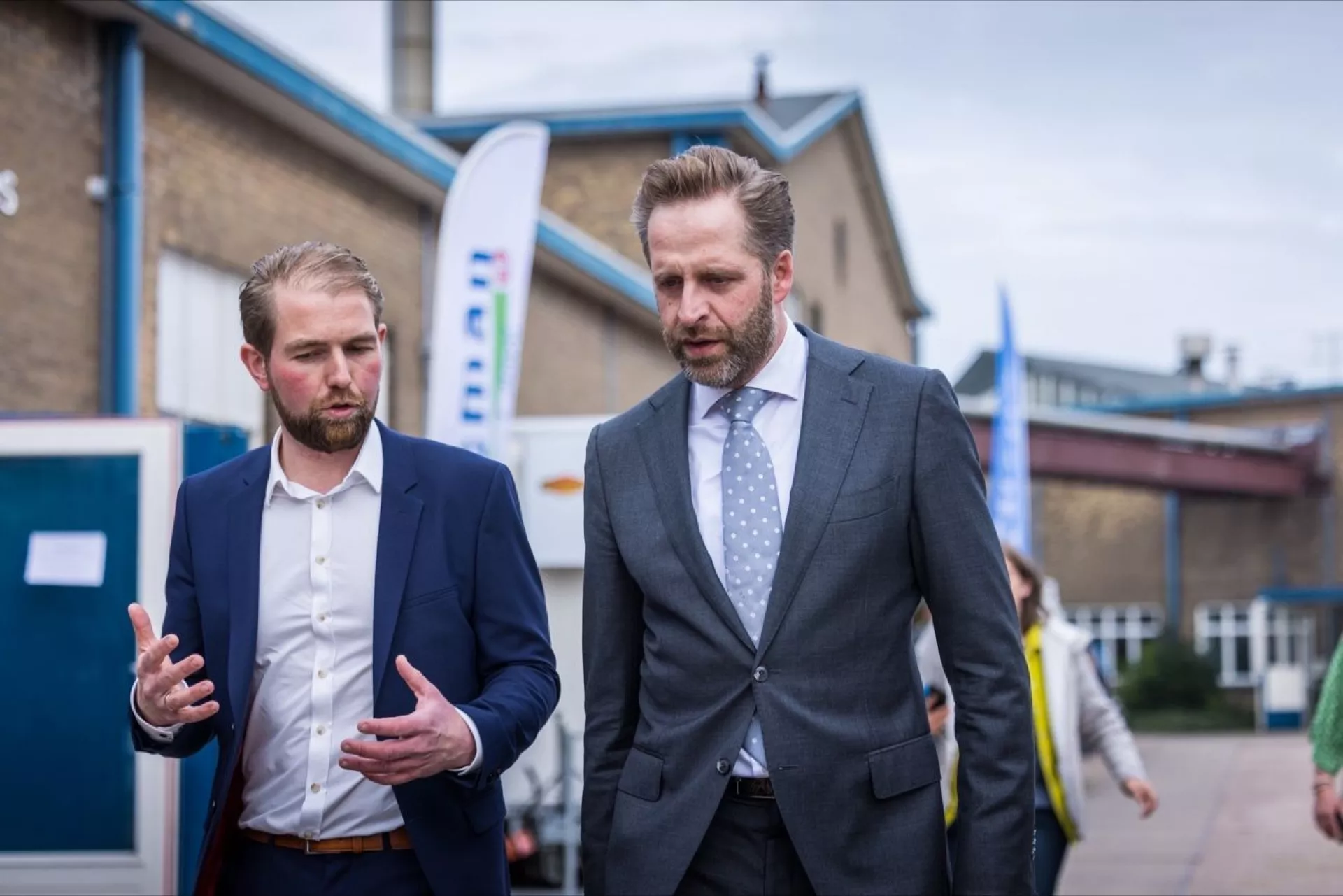 Twee mannen in pakken wandelen buiten een gebouw en praten met elkaar.