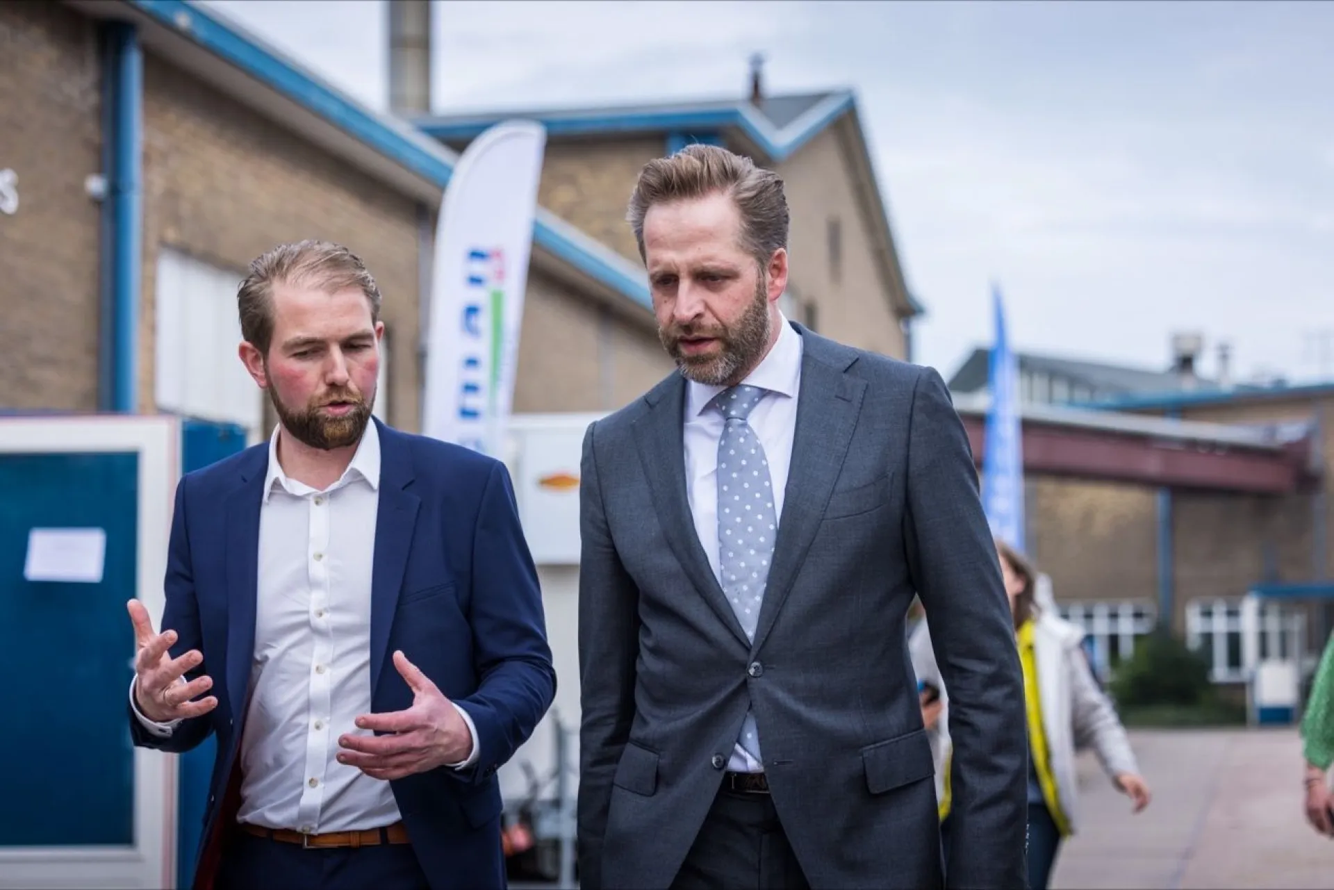 Twee mannen in pakken wandelen buiten een gebouw en praten met elkaar.