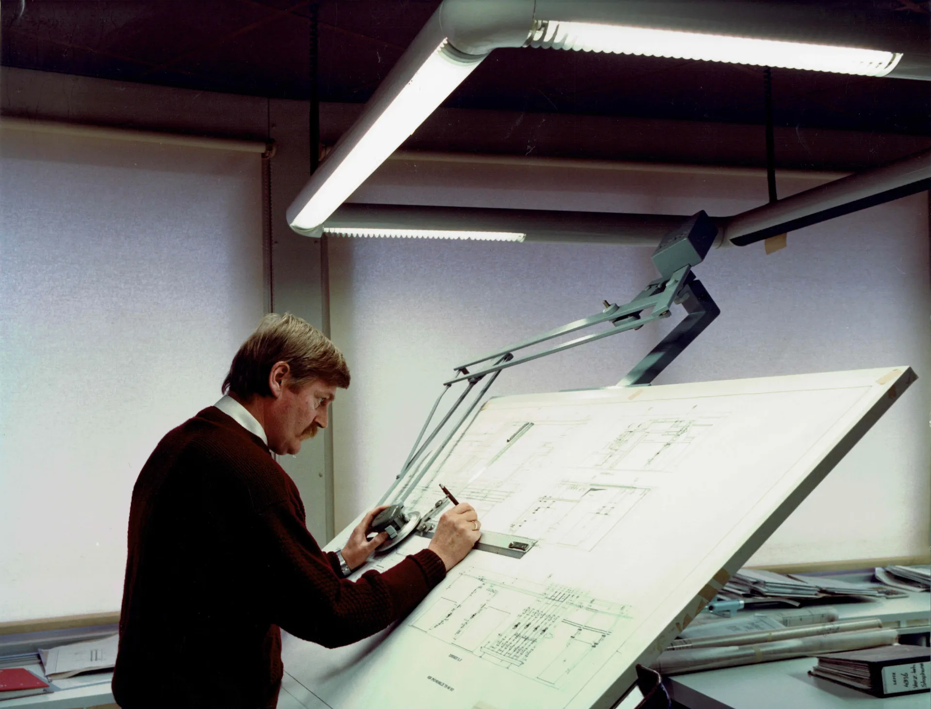 Man werkt aan een tekentafel met bouwkundige ontwerpen. (historische foto)