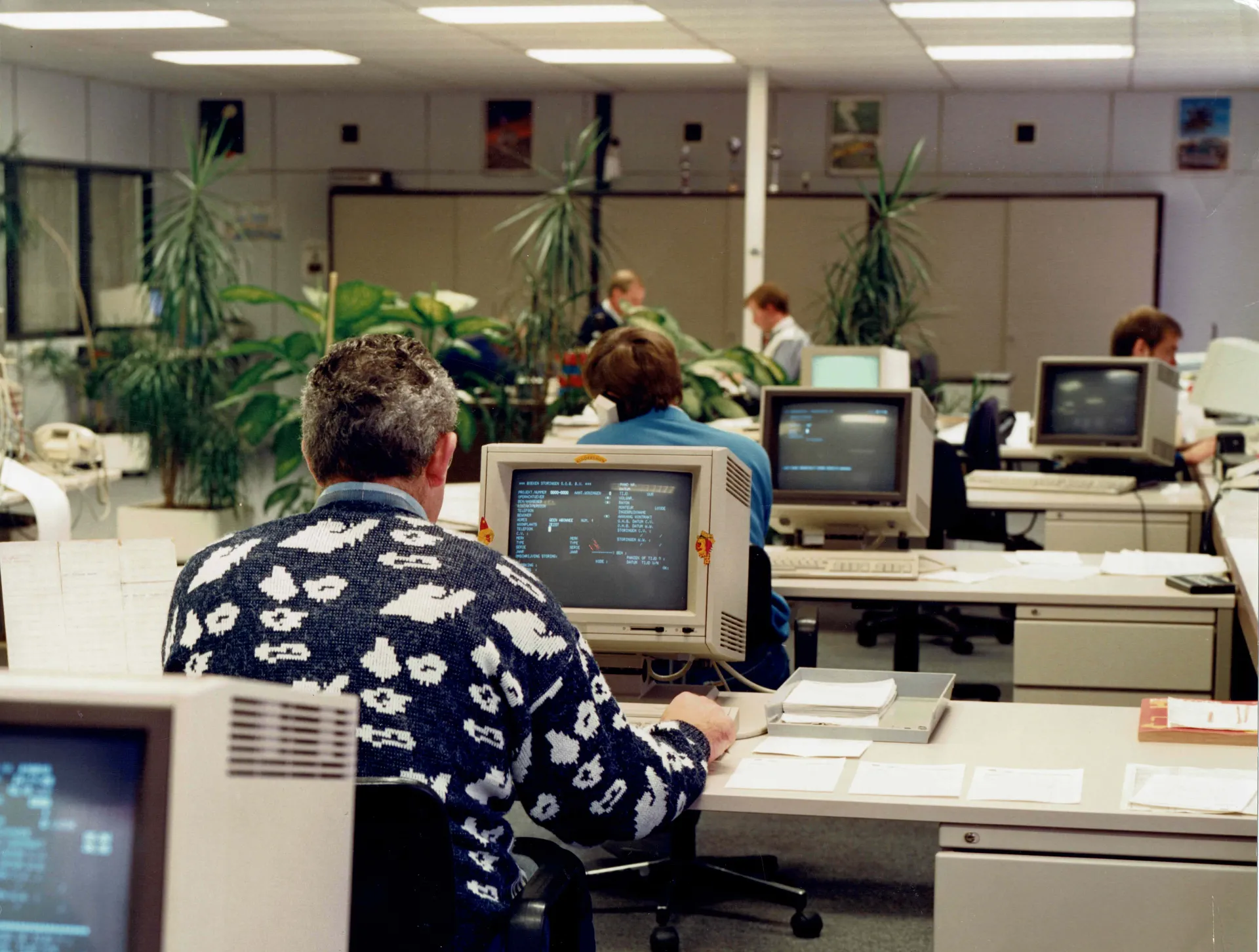 Kantooromgeving met mensen die op oude computers werken.