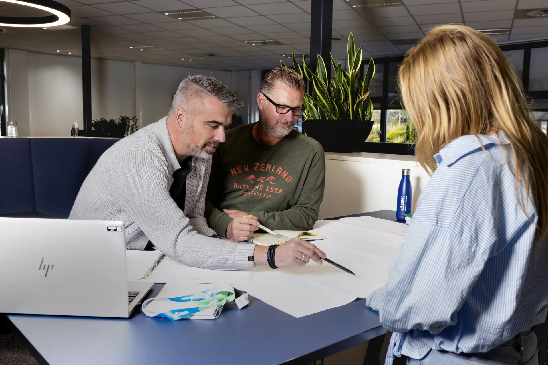Drie mensen werken samen aan een project in een kantooromgeving.