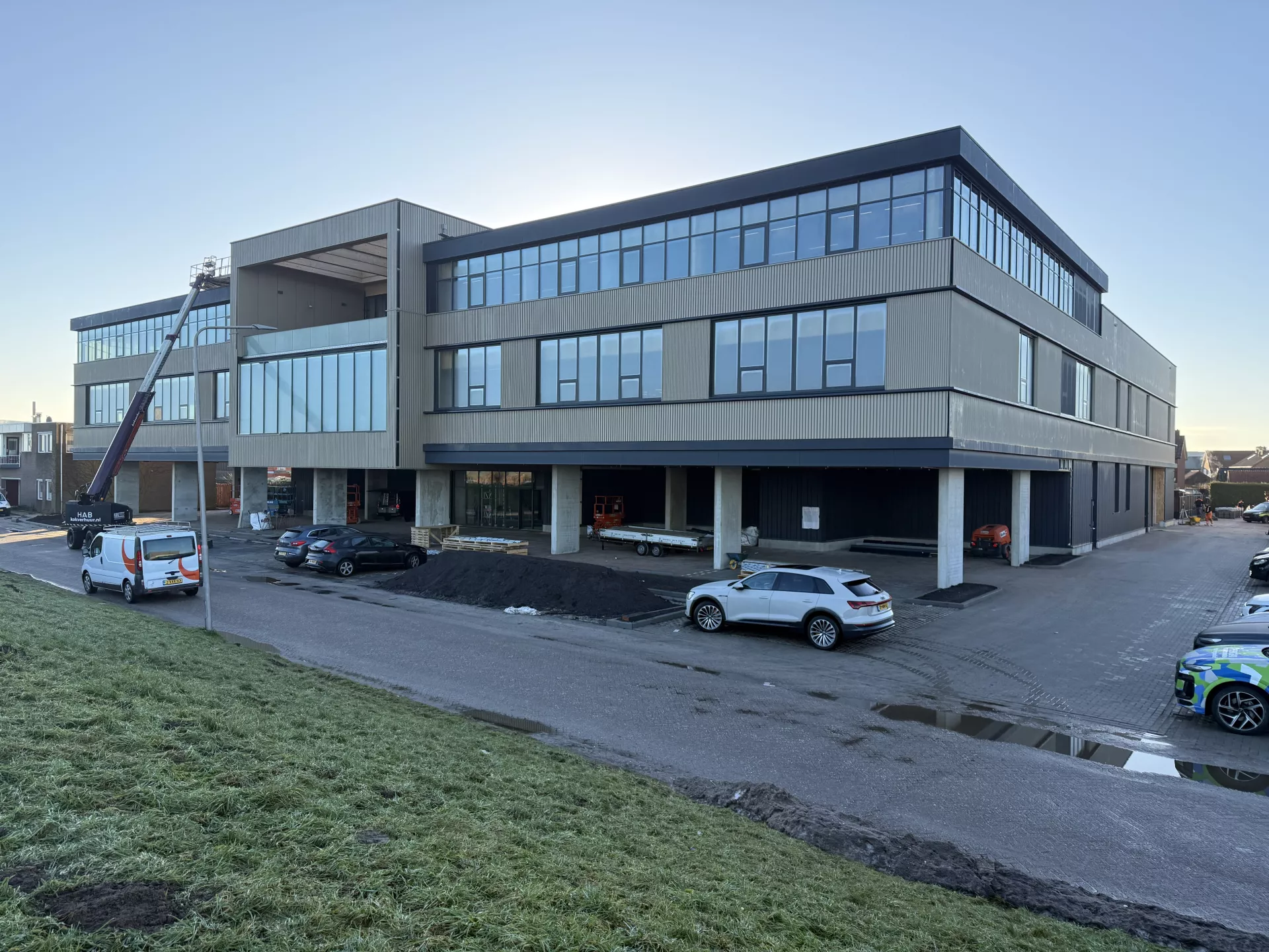 Een modern kantoorgebouw met geparkeerde auto's aan de voorkant.