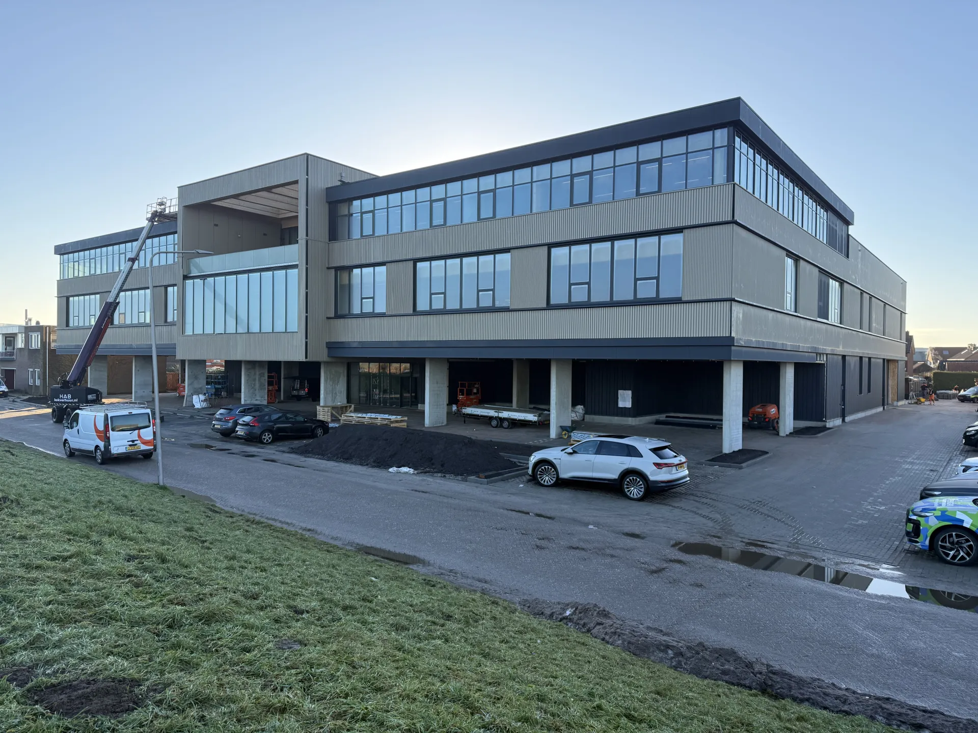 Een modern kantoorgebouw met geparkeerde auto's aan de voorkant.