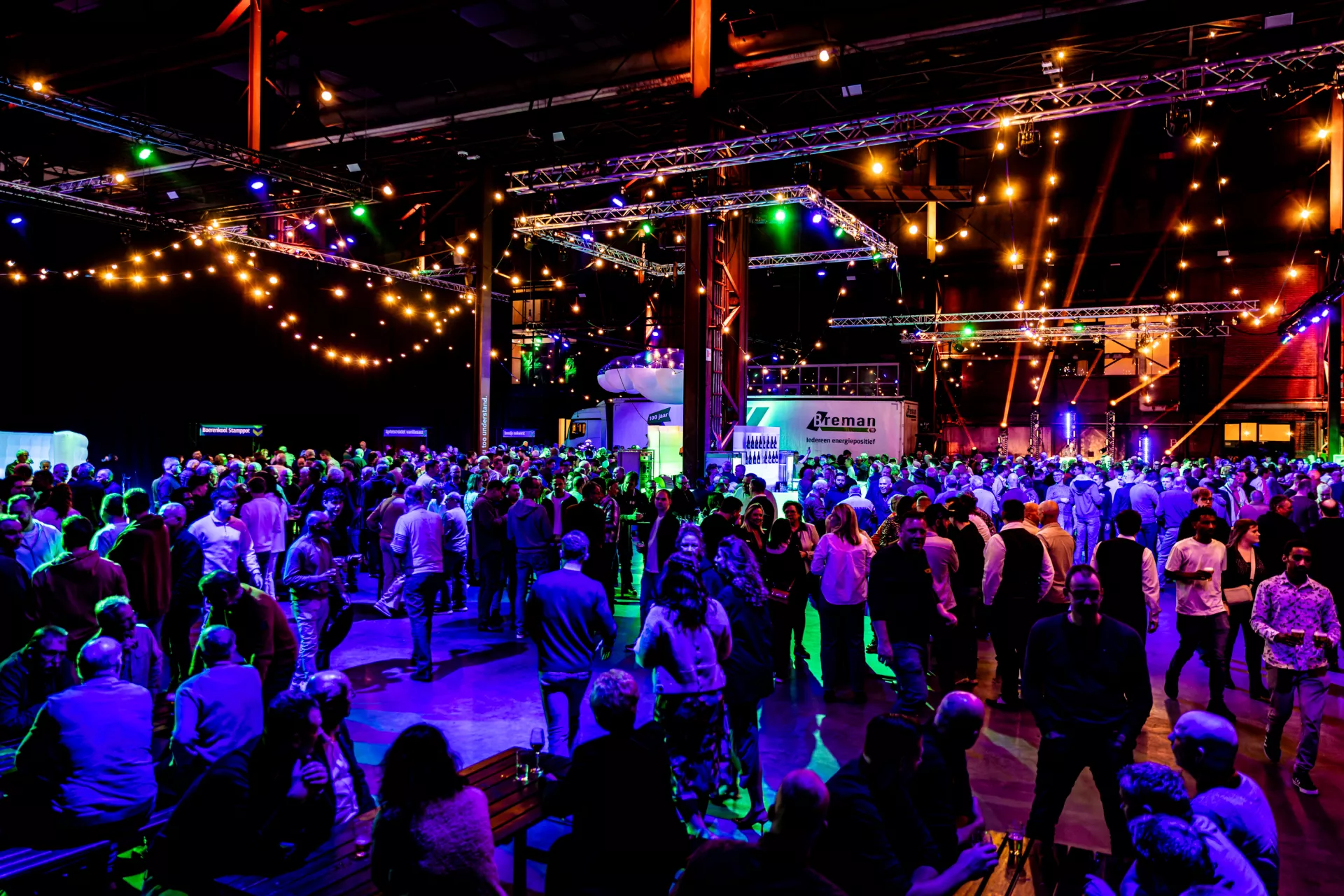 Grote groep mensen op een kleurrijk verlichte evenementlocatie.