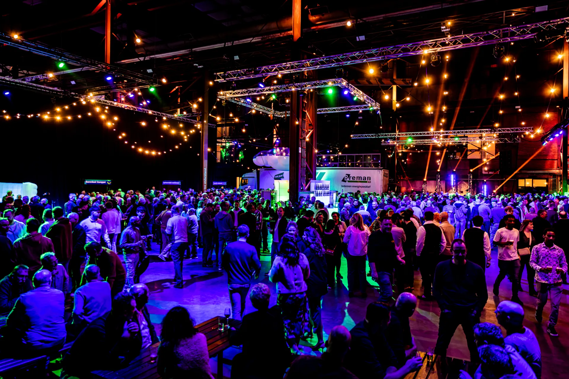 Grote groep mensen op een kleurrijk verlichte evenementlocatie.