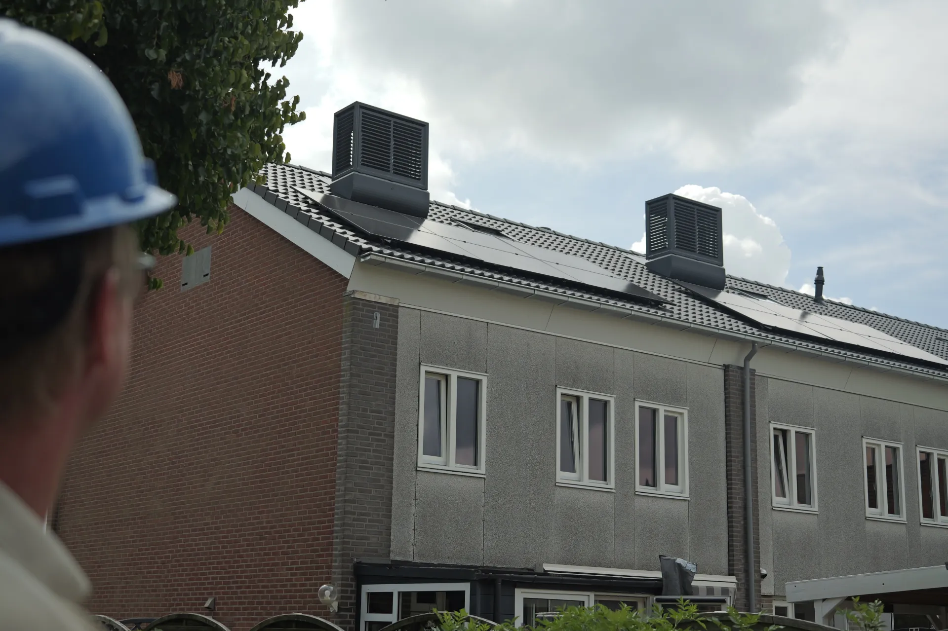 Een persoon met een helm kijkt naar een huis met zonnepanelen op het dak.