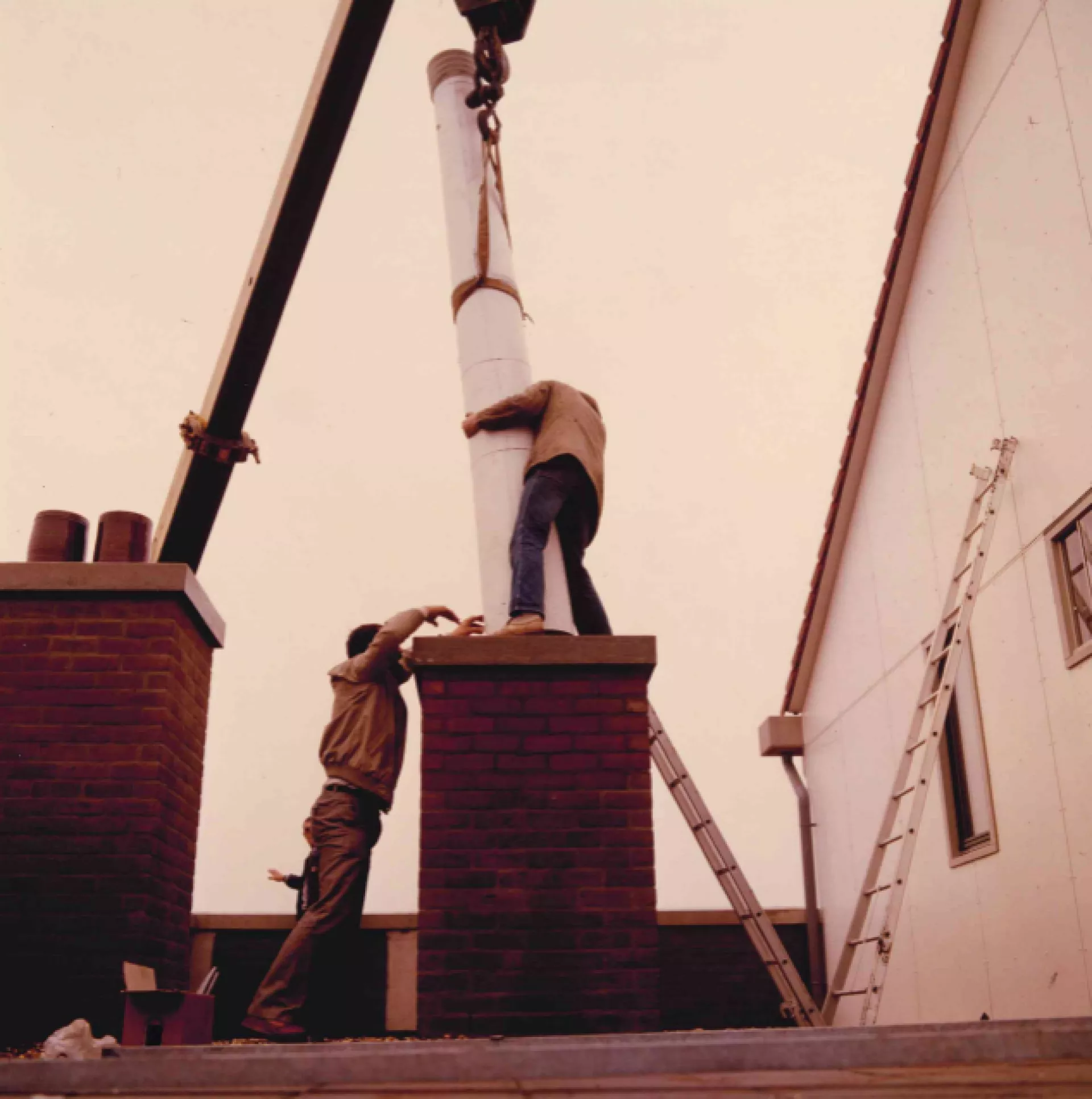 Twee mannen installeren een grote buis op een gebouw. (historische foto)