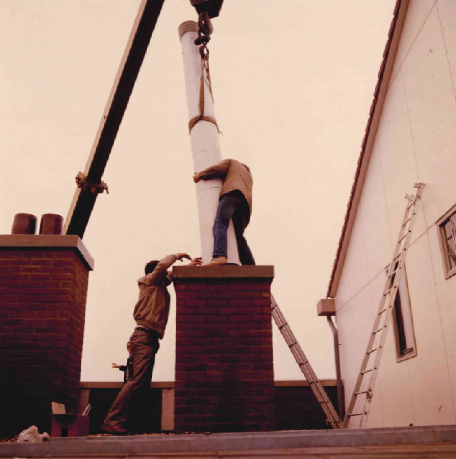 Twee mannen installeren een grote buis op een gebouw. (historische foto)