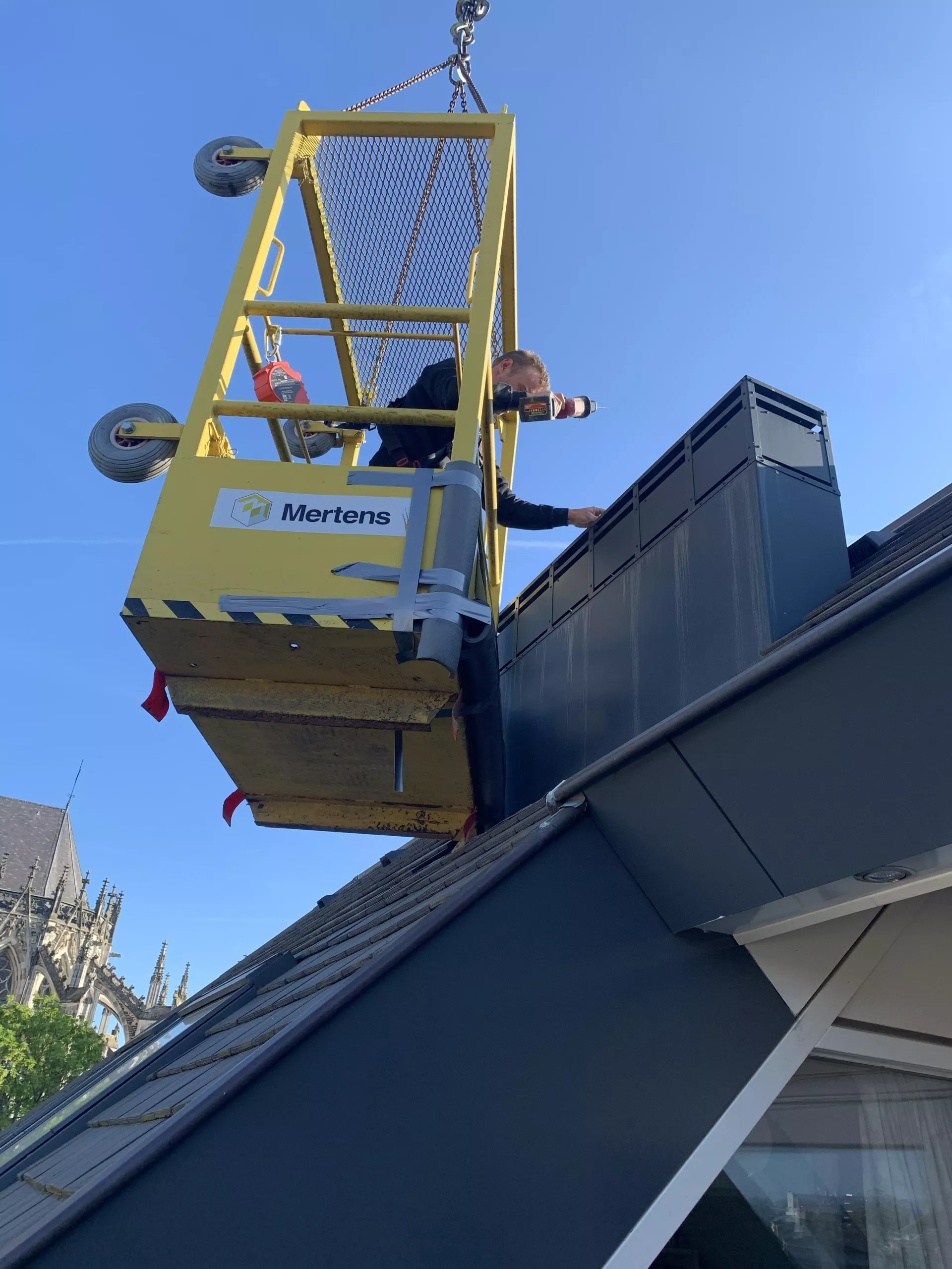 Een persoon in een hijsplatform werkt aan de buitenkant van een gebouw.