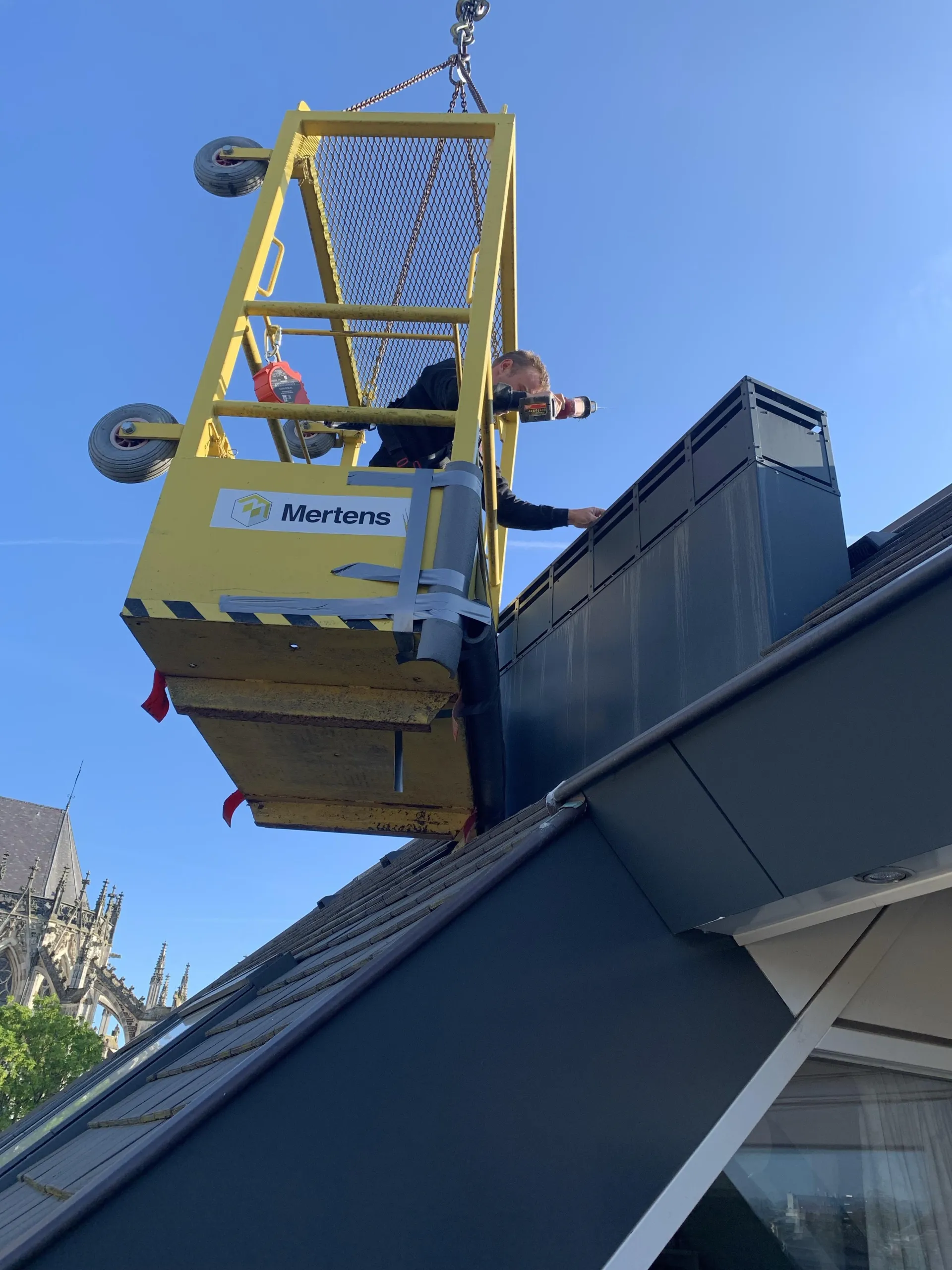 Een persoon in een hijsplatform werkt aan de buitenkant van een gebouw.