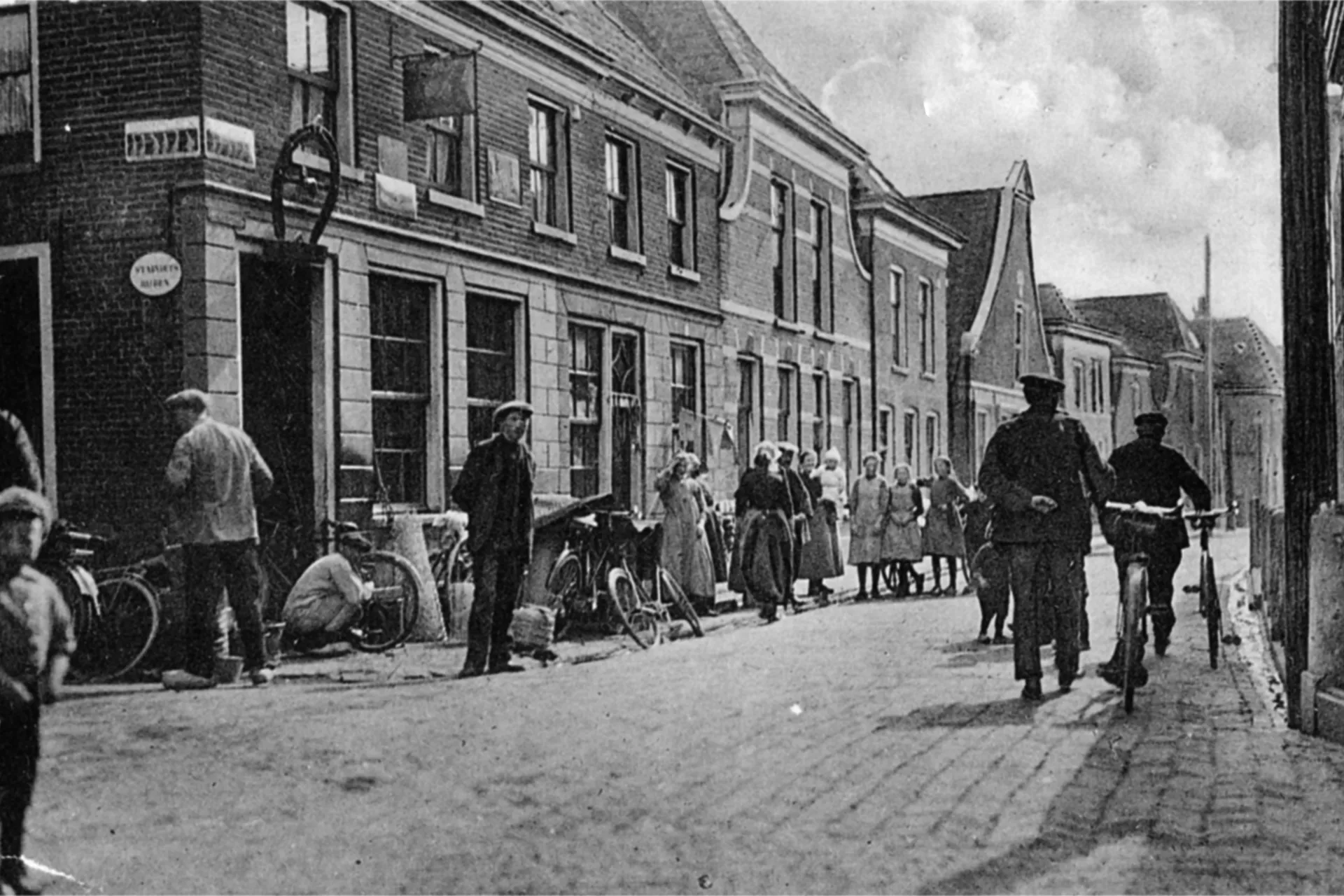 Historisch straatbeeld met mensen en fietsen voor winkels en woningen